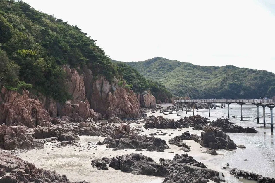무의도 하나개해수욕장의 썰물 때 풍경. 붉은 암벽과 갯벌 바위가 드러나 있고 오른쪽으로 바다 위 나무 데크 산책로가 이어진다